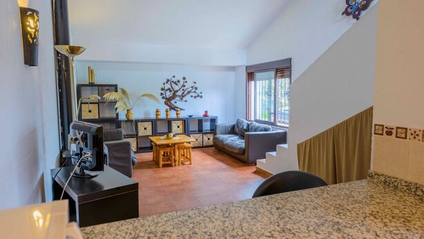 A modern living room with a sofa, a dining table, and a staircase. - Casa Diego Piña Júzcar by Ruralidays (Málaga)