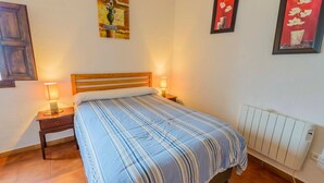A bedroom with a bed, two bedside tables, a nightstand, a radiator, and two wall-mounted lamps. - Casa Diego Piña Júzcar by Ruralidays (Málaga)
