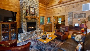 A log cabin interior with a stone fireplace, leather furniture, and a television.