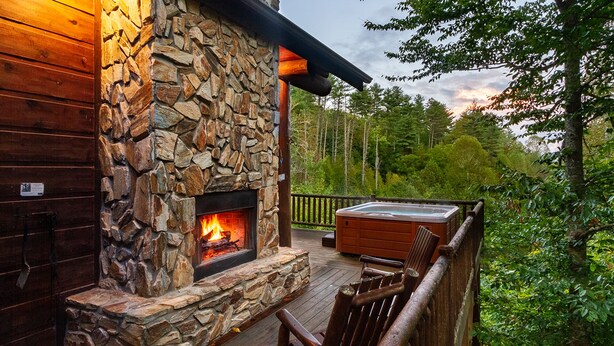 A stone fireplace with a fire, wooden deck, and a hot tub.