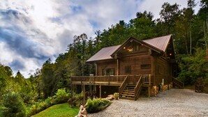 A log cabin with a deck, surrounded by a forest.