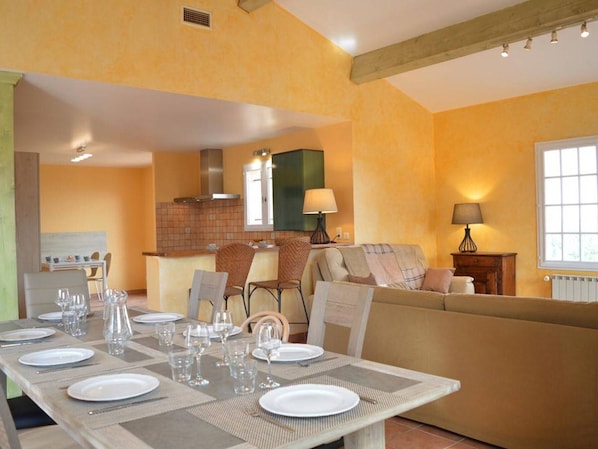 Un coin repas avec une table dressée pour six personnes, un canapé et une cuisine en arrière-plan.