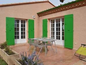 Une terrasse avec une table et des chaises, des volets verts et un sol carrelé.
