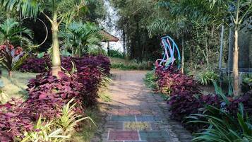 Un chemin de jardin dallé, bordé d’une végétation luxuriante et agrémenté d’une sculpture métallique décorative.