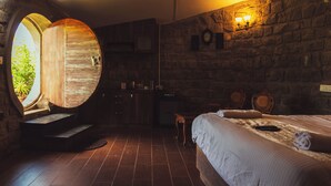 Una habitación rústica con un gran puerta de madera, una cama con cabecera, una pared de piedra y una pequeña mesa.