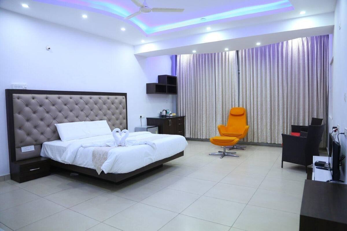 A modern hotel room with a large bed, a desk, an orange chair, and a TV.