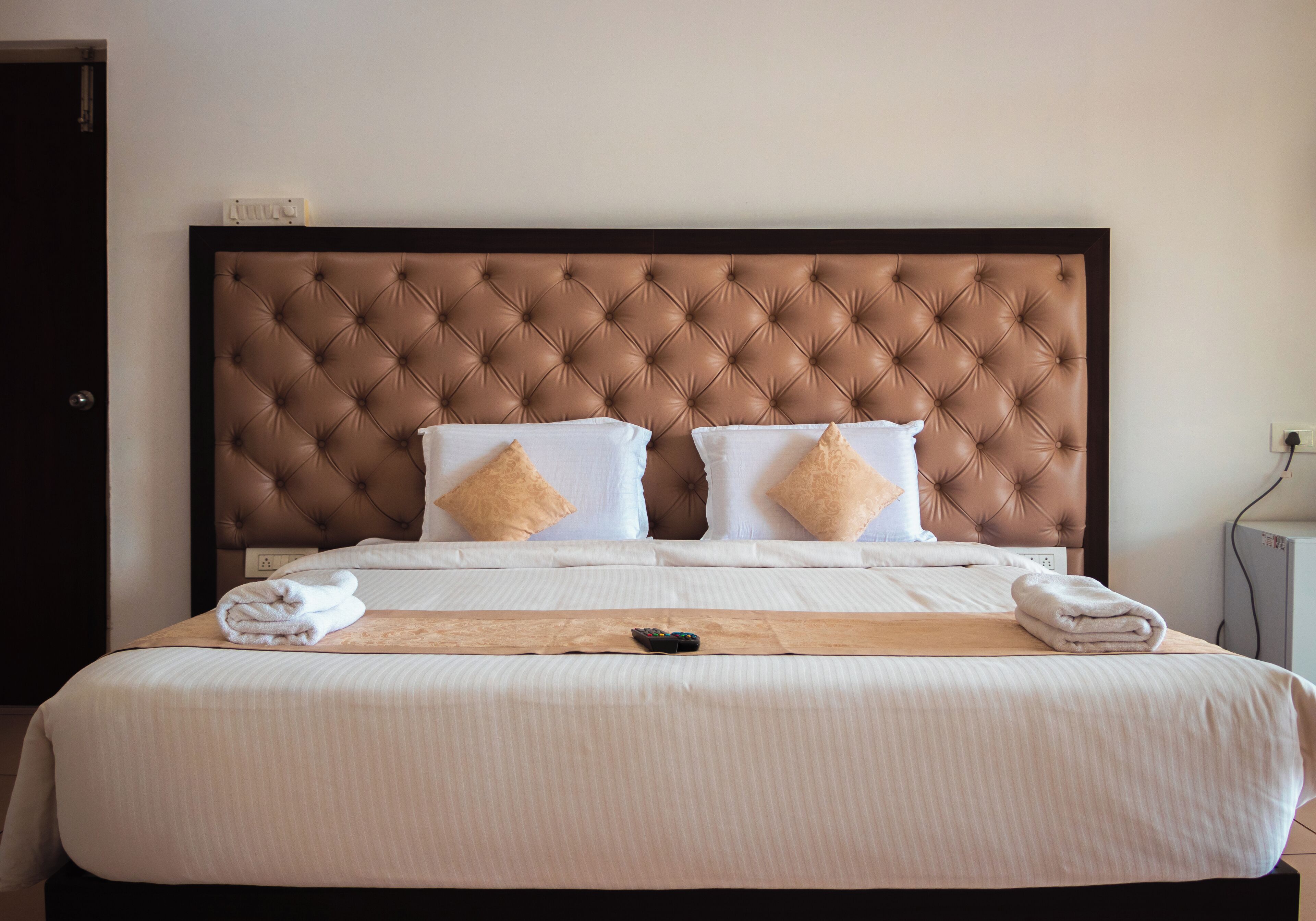 Una cama bien hecha con un cabecero capitonado, ropa de cama blanca y dos almohadas color beige.