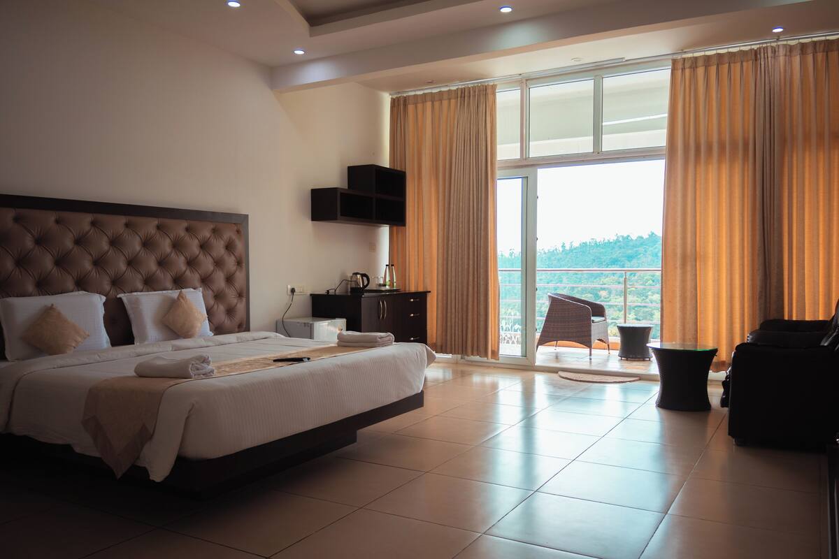 A spacious hotel room with a large bed, a balcony with a view, and a seating area.