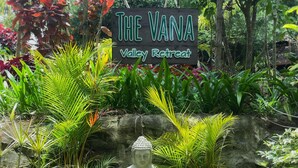 «The Vana Valley Retreat» -niminen kyltti, jonka ympärillä on vehreää kasvillisuutta ja jonka lähellä on Buddhan patsas.