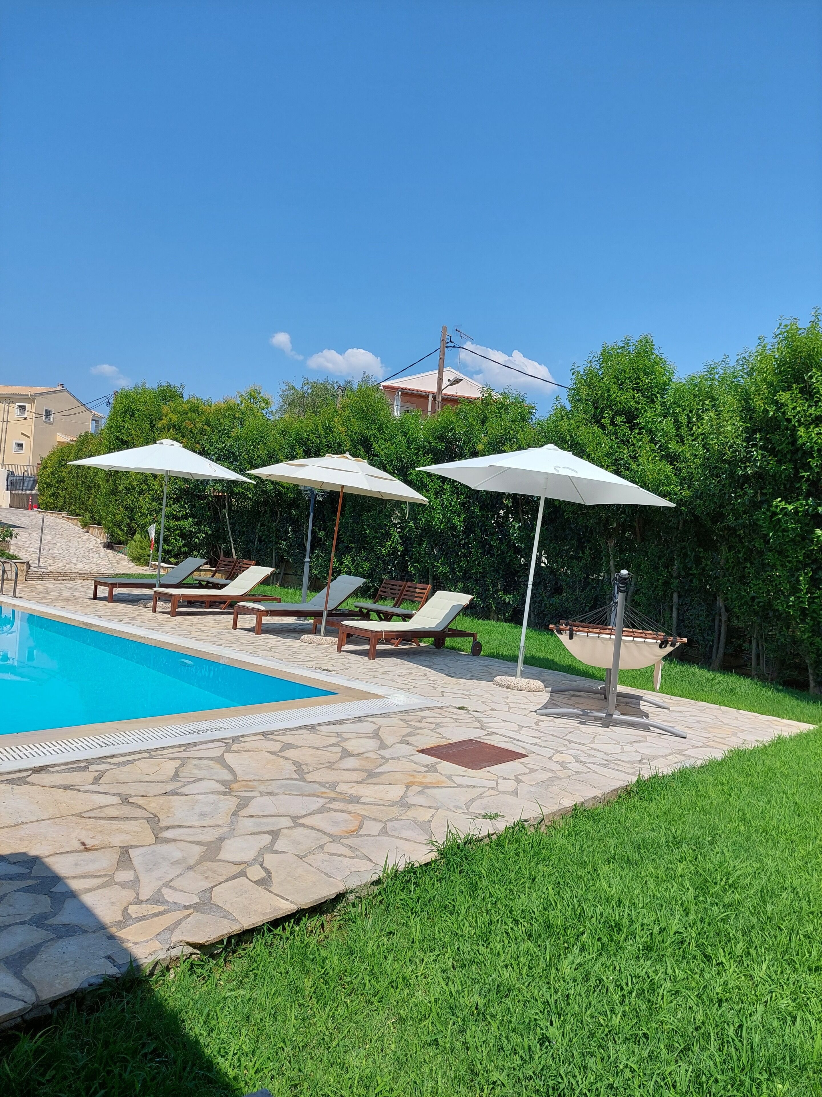 Una piscina con sillas de descanso y sombrillas, rodeada de baldosas de piedra y césped.