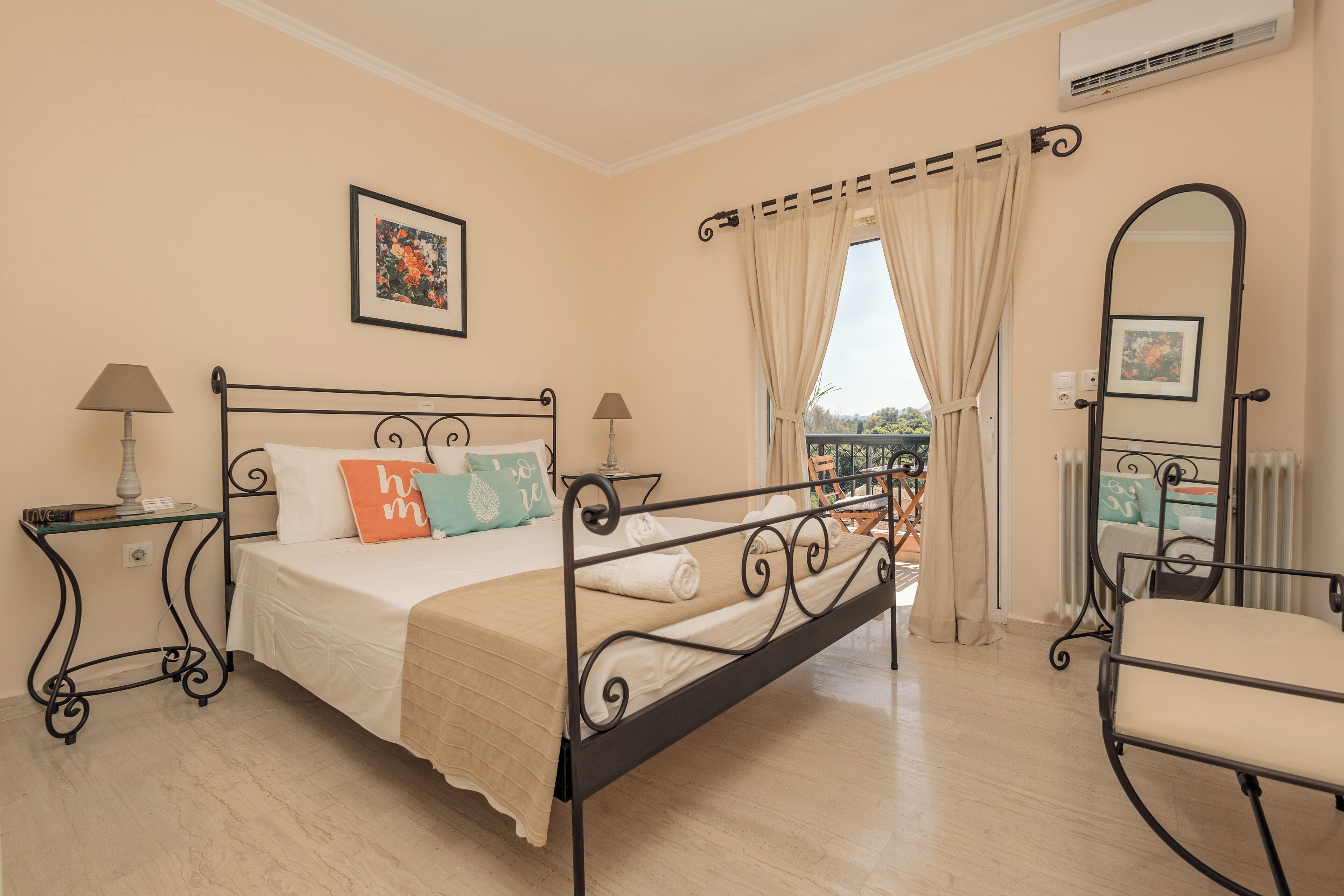Un dormitorio con cama, dos mesitas de noche, una silla, un ventanal con cortinas y un espejo.