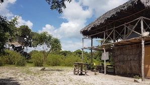 A rustic thatched-roof structure with a wooden table and a bench, surrounded by greenery and trees. - Mida Creek Nature Camp (Watamu)