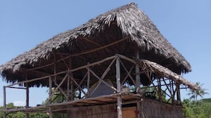 A thatched-roof hut with a simple wooden frame, a small bench, and a door. - Mida Creek Nature Camp (Watamu)