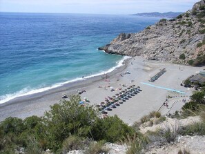 A beach with rows of umbrellas and sun loungers, rocky cliffs, and the ocean. - Beautiful house- Albaicín- City center. Parking for large cars (granada)