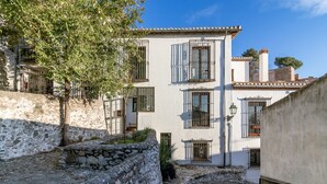 Un patio con paredes de piedra, un árbol y un edificio con ventanas con rejas y techo de tejas.