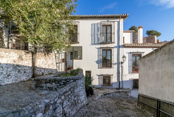 A courtyard with stone walls, a tree, and a building with barred windows and a tiled roof. - Beautiful house- Albaicín- City center. Parking for large cars (granada)
