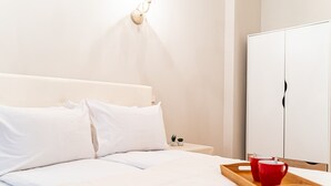 A neatly made bed with white linens and pillows, a bedside table with a red mug and a tray, and a white wardrobe in a minimalist room. - WINWINSTAY Art Nouveau Lumiere Residence (Riga)