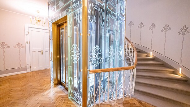 A modern interior with a herringbone wooden floor, a glass partition with decorative etching, and a staircase with a wooden railing. - WINWINSTAY Art Nouveau Lumiere Residence (Riga)
