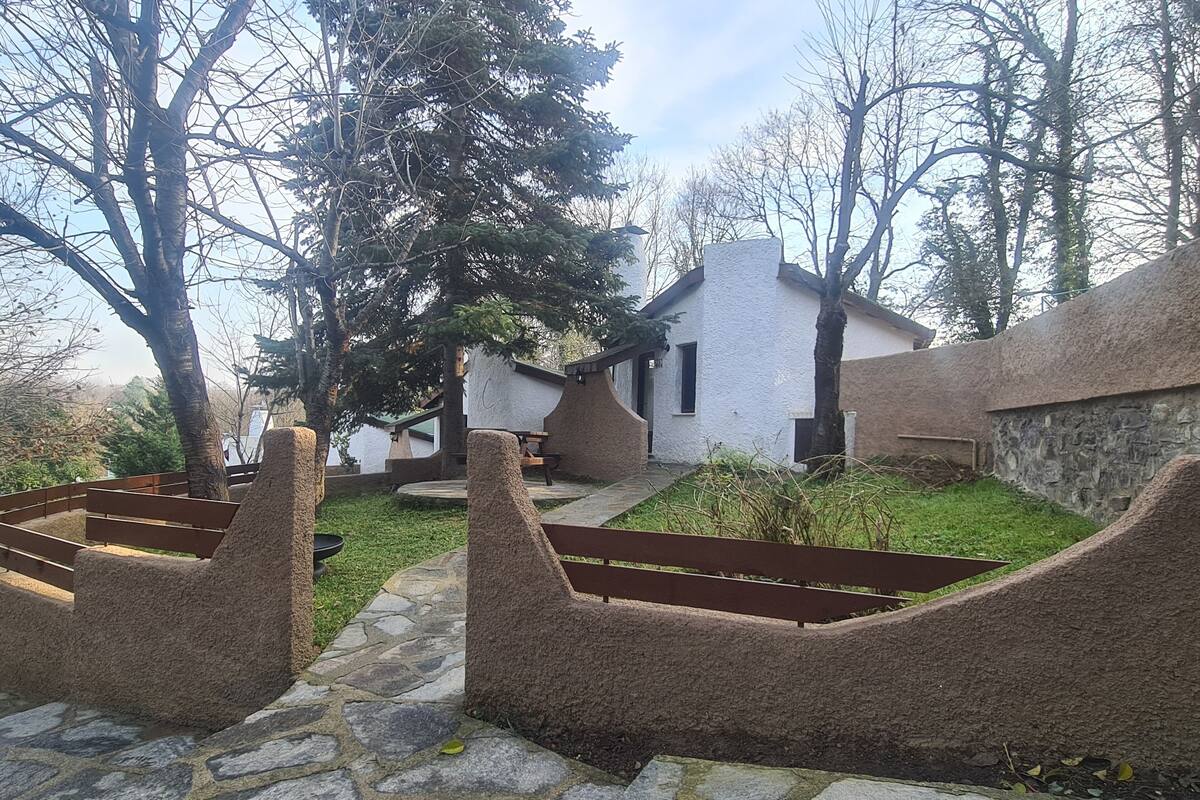 A rustic outdoor area with stone pathways, wooden benches, and a white building with a chimney.