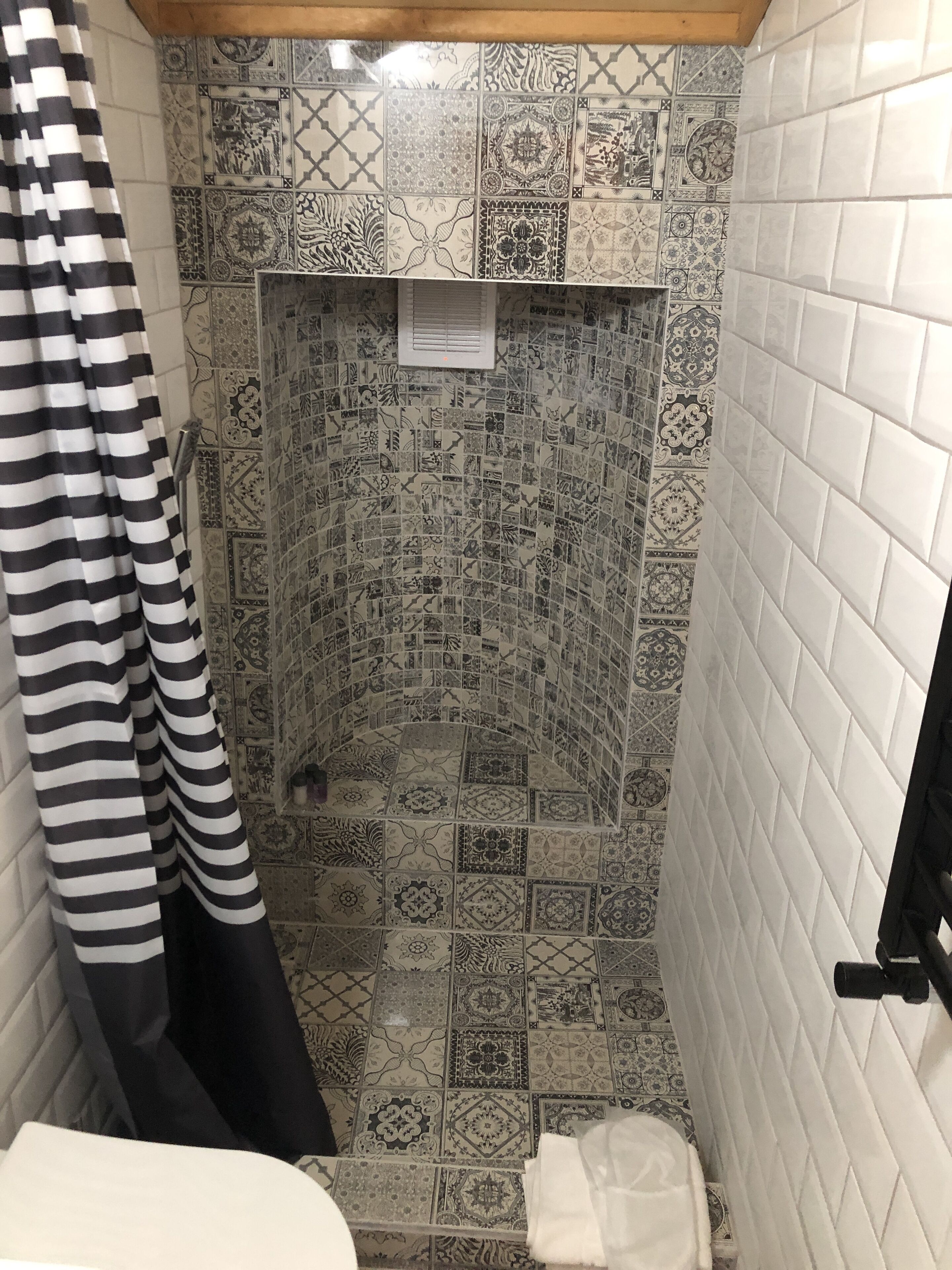A bathroom with patterned tiles, a shower, and a striped curtain.