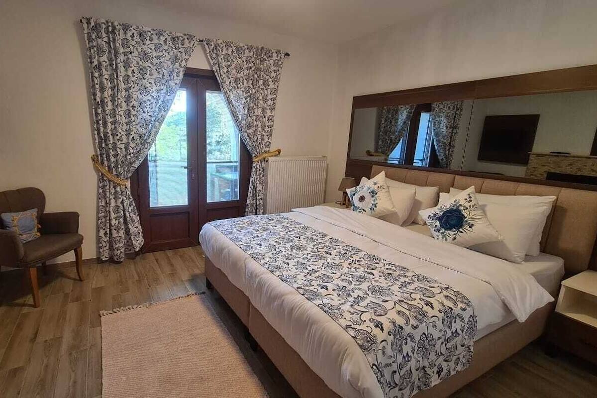 A bedroom with a large bed, a chair, a TV, and a window with curtains.