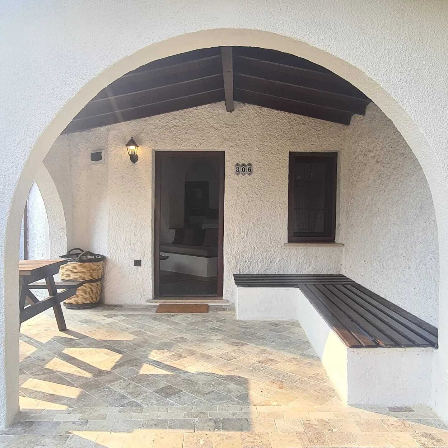 A covered patio area with a bench, a door, and a wall-mounted light fixture.