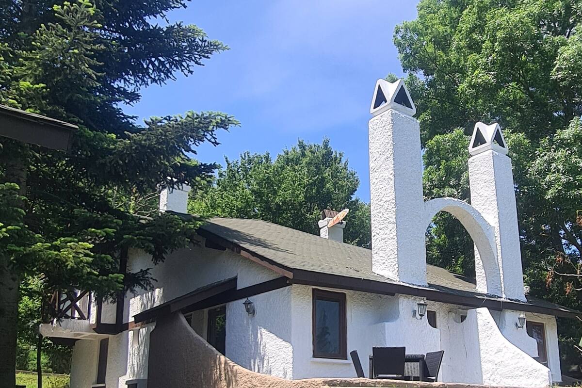 A rustic building with a stone chimney, a picnic table, and a stone wall.