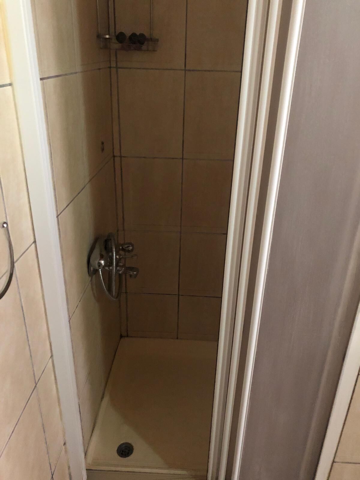 Une petite cabine de douche carrelée, équipée d’une seule pomme de douche et d’un drain.