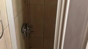 Une petite cabine de douche carrelée, équipée d’une seule pomme de douche et d’un drain.