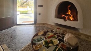 A cozy room with a stone fireplace, a dining table set with various dishes, and a view of the outdoors through an open door. - Polonezköy Country Club & Accommodation in the Wildlife Park (Beykoz)