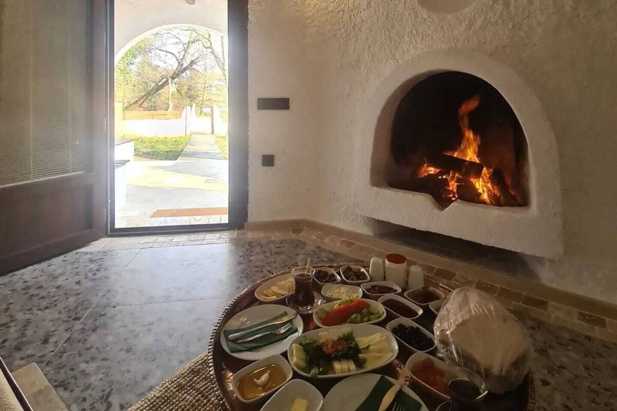 A cozy room with a stone fireplace, a dining table set with various dishes, and a view of the outdoors through an open door.