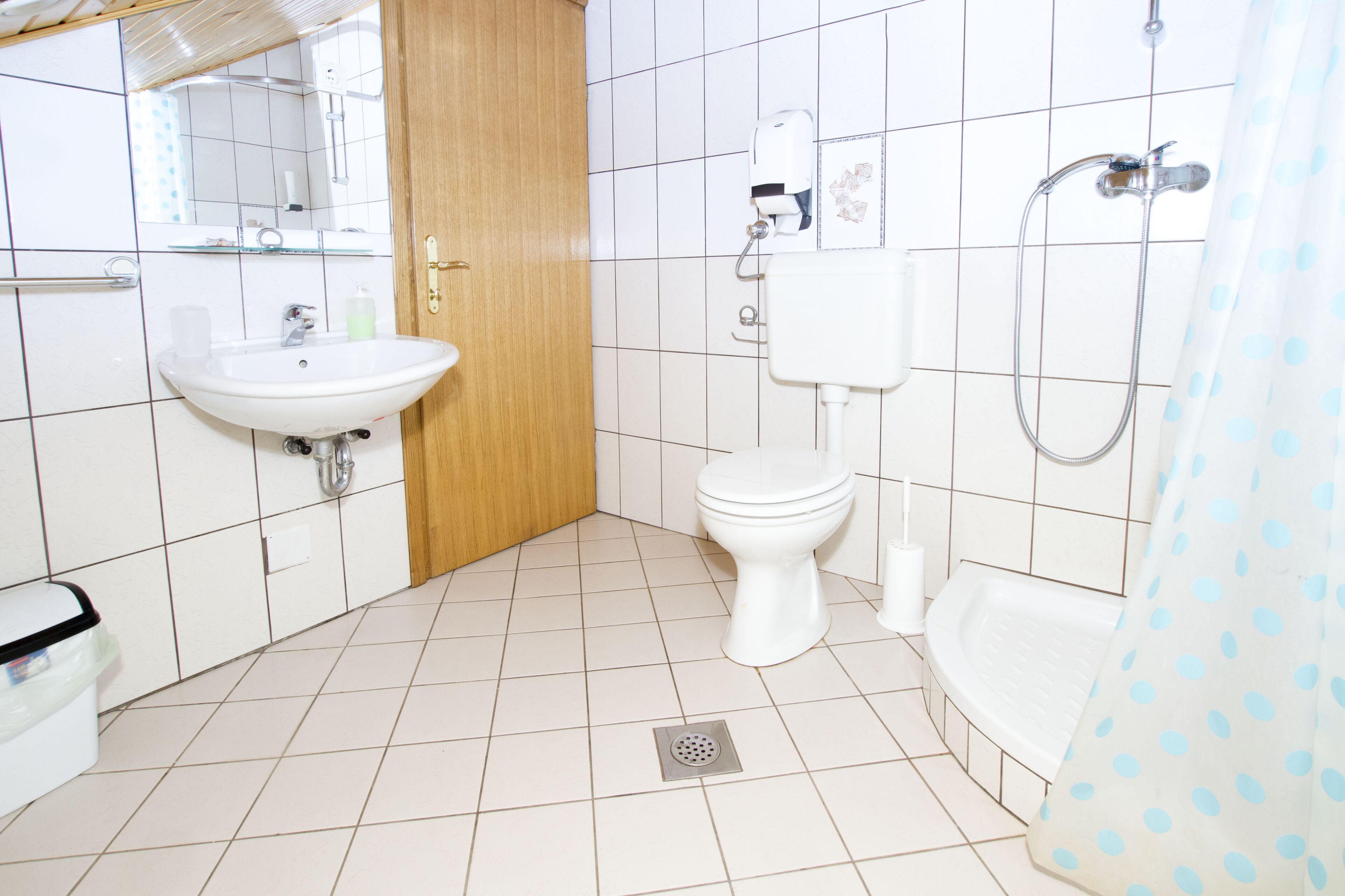 Un baño con lavabo, inodoro, ducha y puerta de madera.