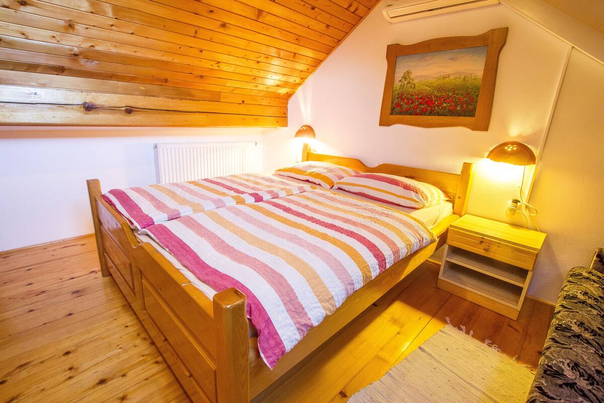 A wooden bed with a striped bedspread, a nightstand with a lamp, and a painting on the wall.