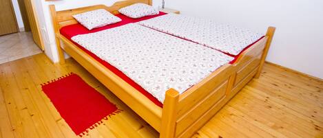 A wooden bed with a red and white bedspread, a wooden headboard, and a red rug on a wooden floor.