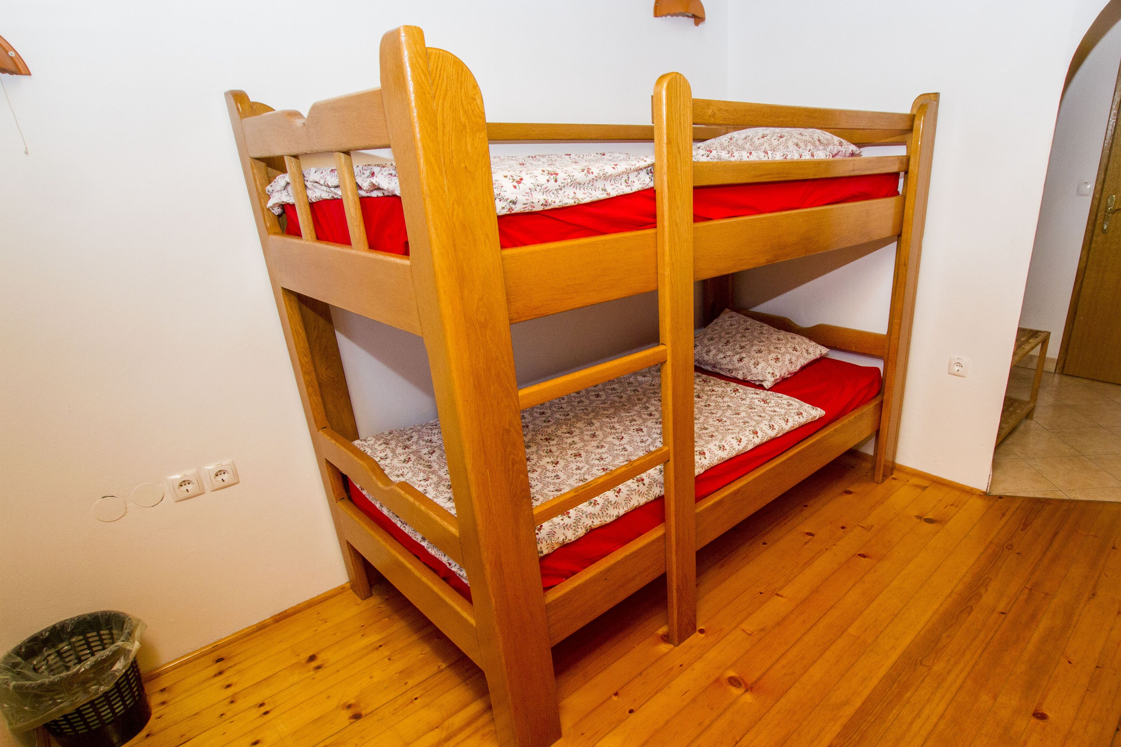 Un lit superposé à trois niveaux, avec une structure en bois et une literie rouge.