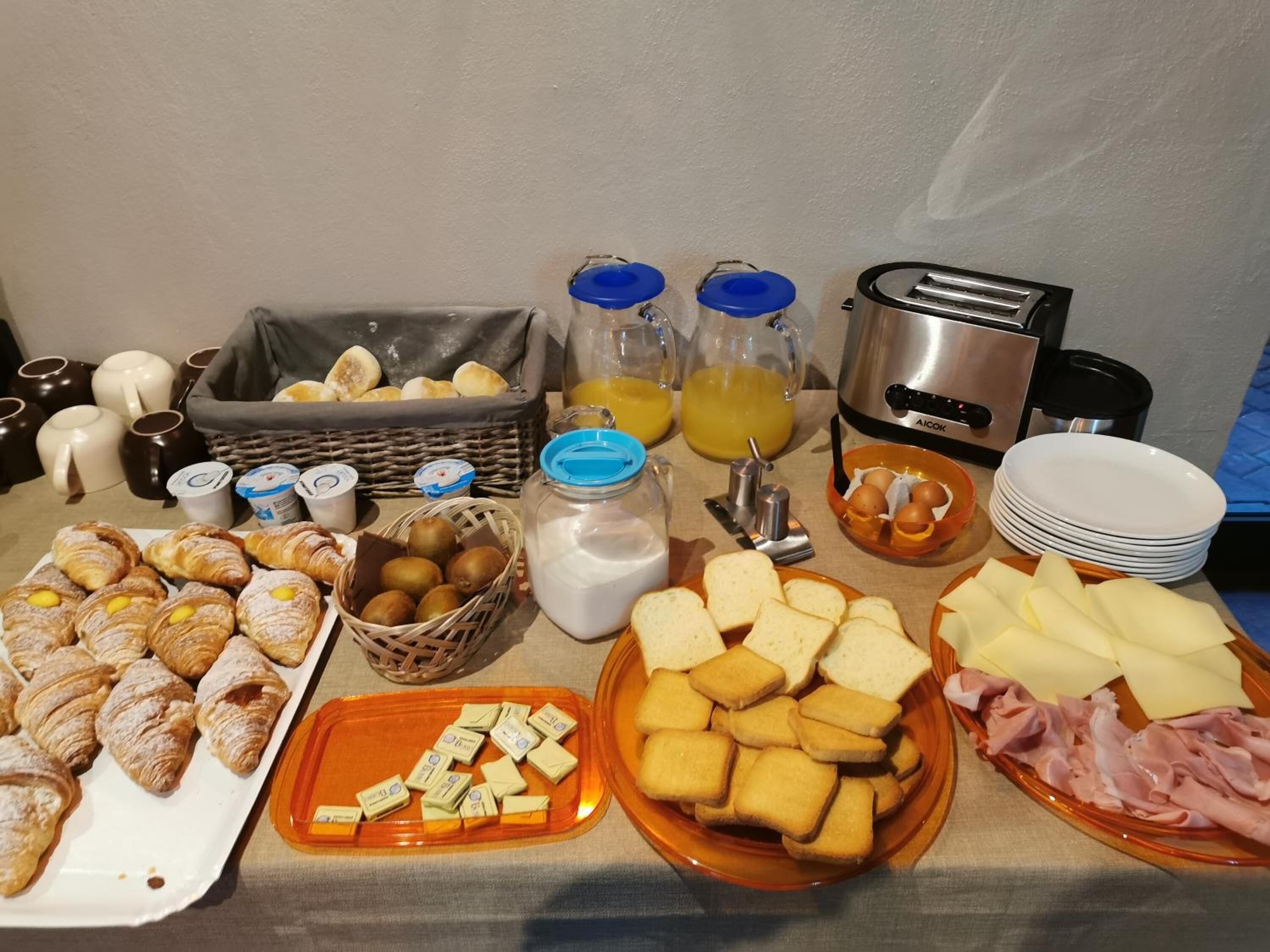A breakfast buffet with pastries, bread, cheese, ham, and beverages.