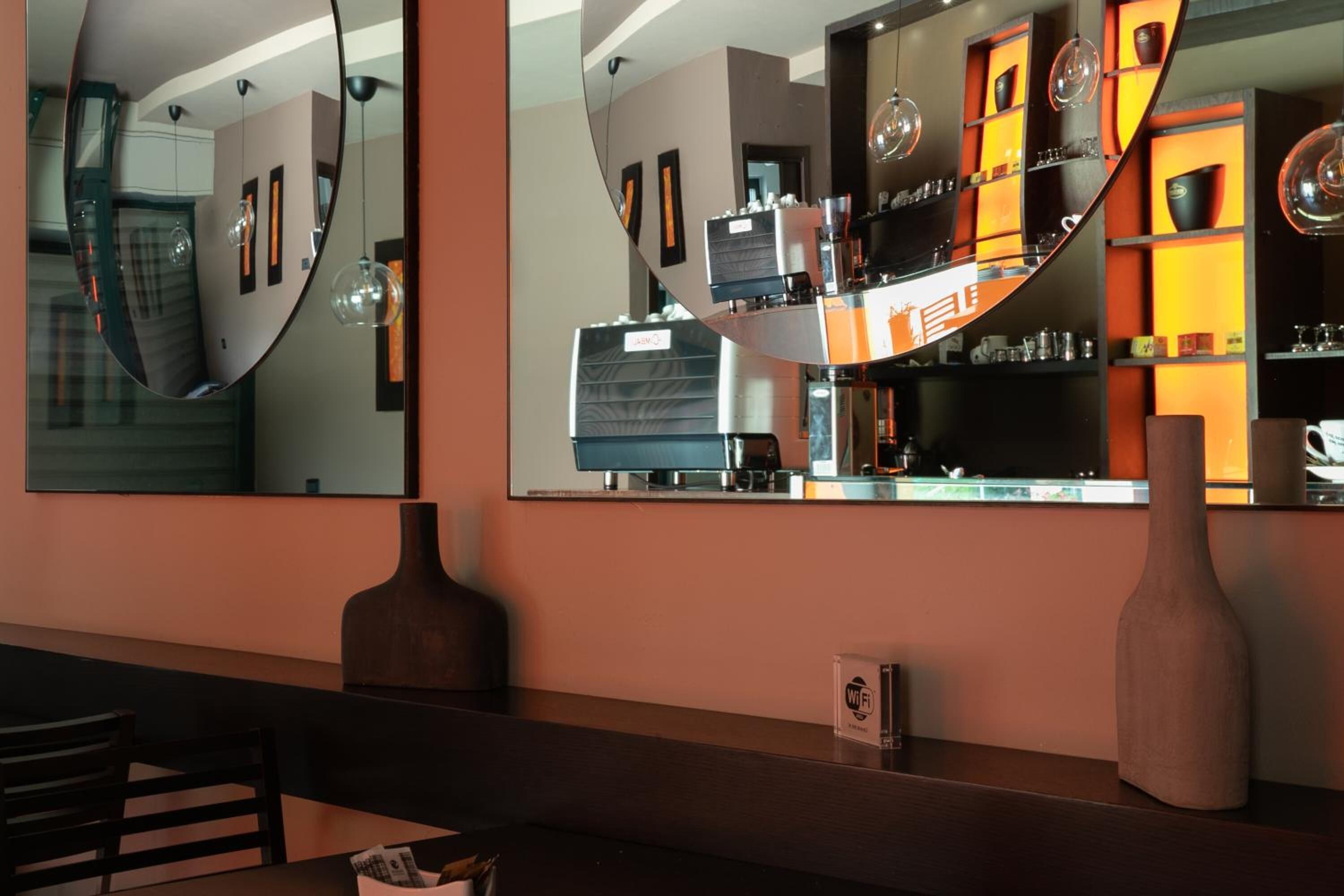 A modern bar area with a curved mirror reflecting the interior, a coffee machine, and shelves with various items.