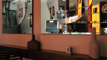 A modern bar area with a curved mirror reflecting the interior, a coffee machine, and shelves with various items.