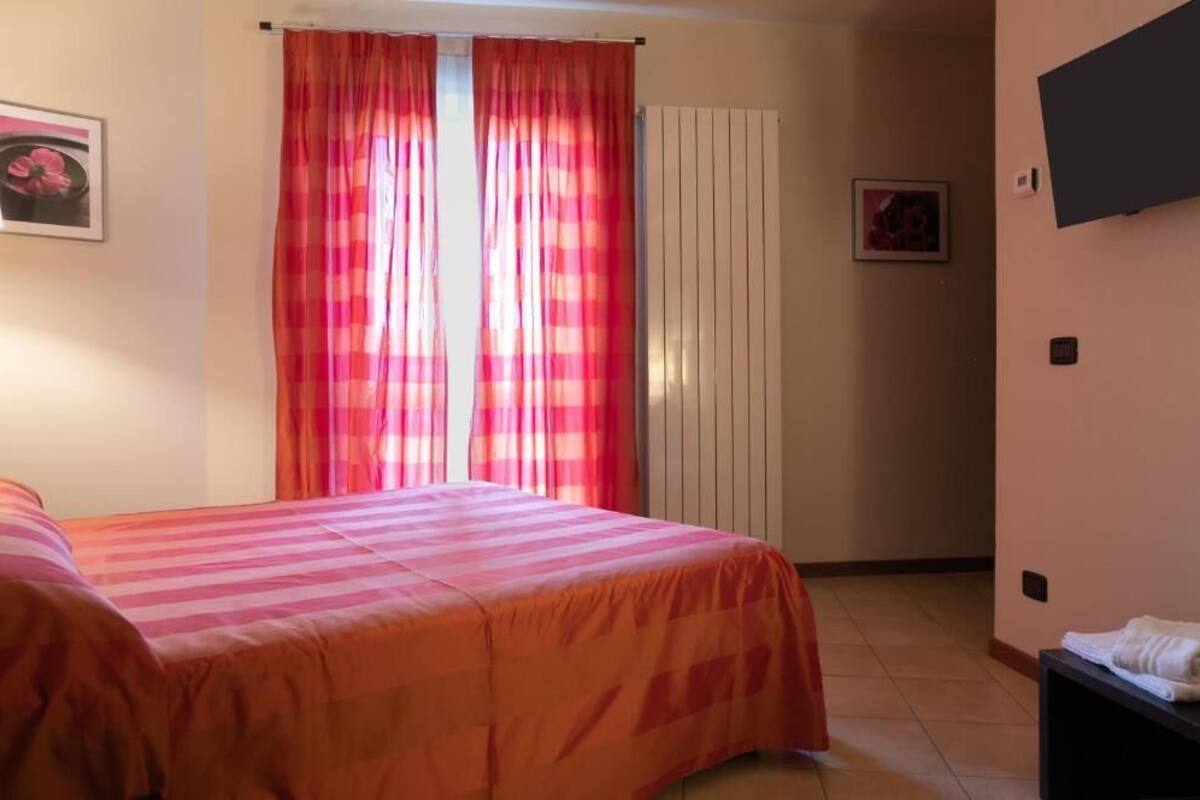A bedroom with two beds, a window with pink curtains, a radiator, and a wall-mounted TV.