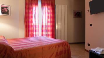 Ein Schlafzimmer mit zwei Betten, einem Fenster mit rosa Vorhängen, einem Heizkörper und einem an der Wand befestigten Fernseher.