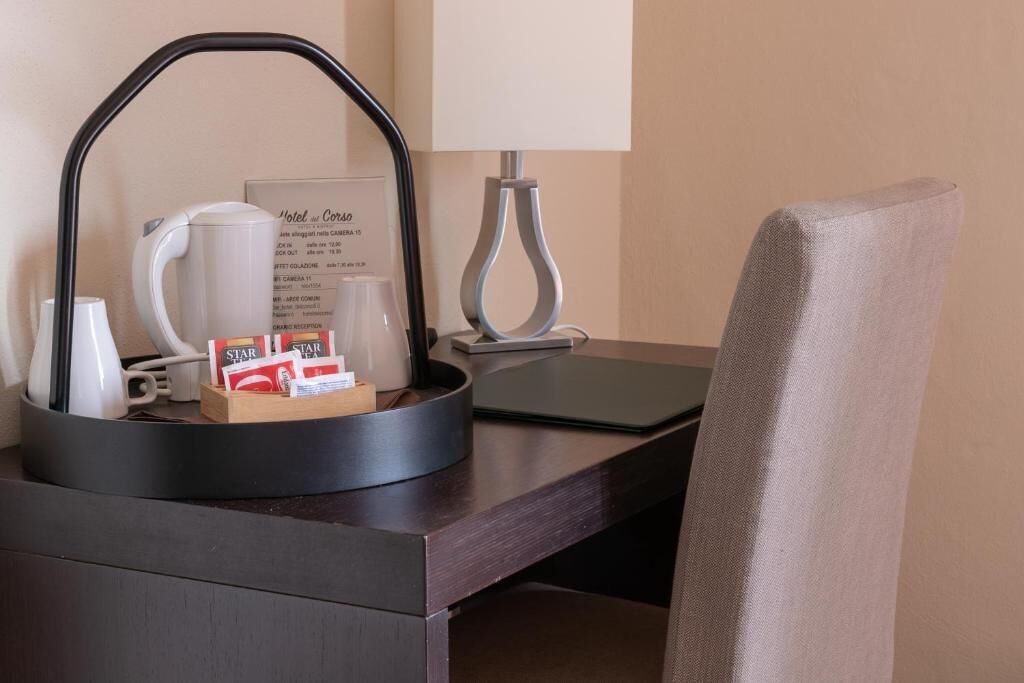 A hotel desk with a coffee maker, cups, a tray with coffee packets, a menu, and a lamp.