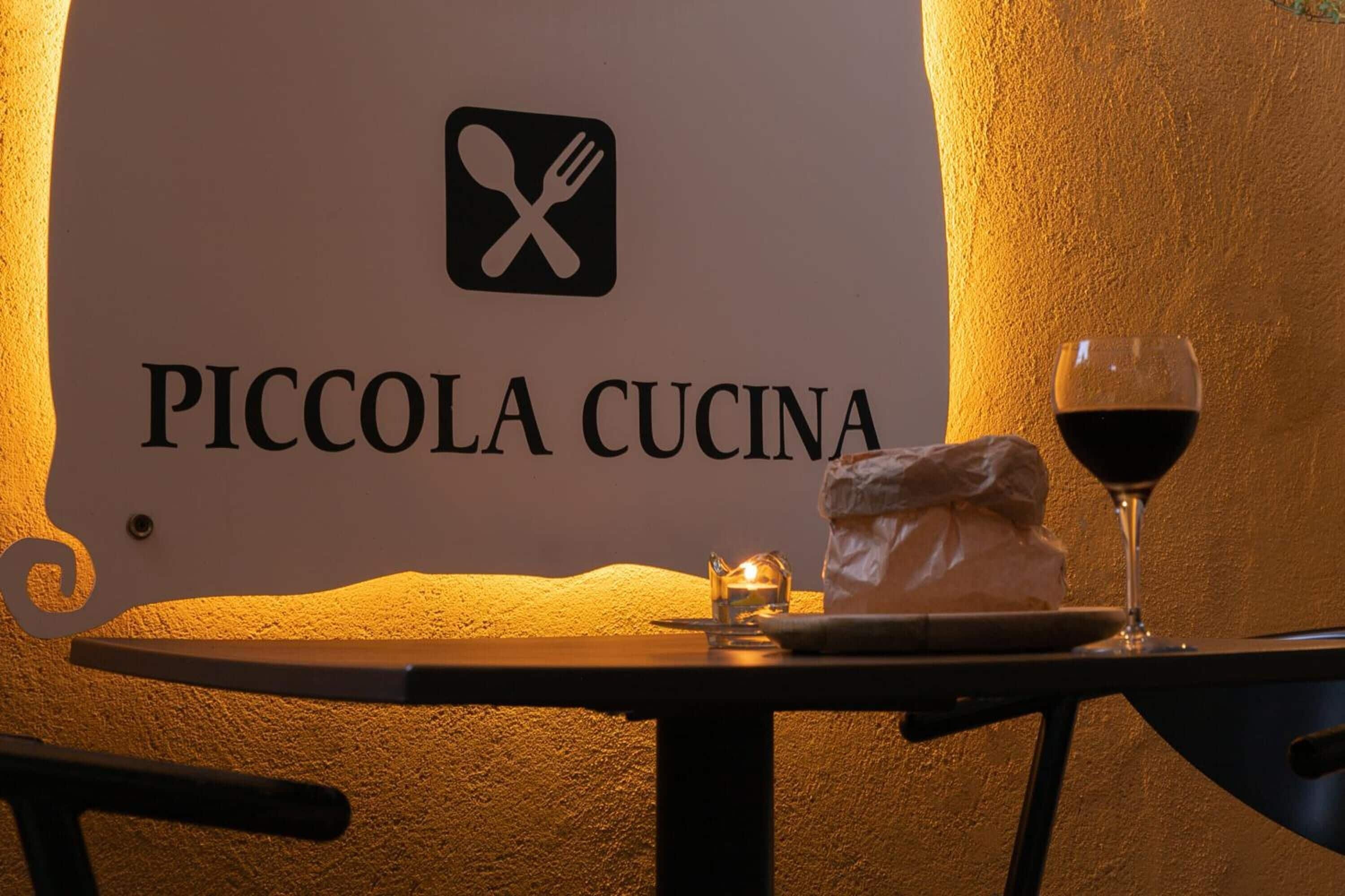 Una mesa con una copa de vino tinto y un plato de comida, frente a una pared con un letrero que dice 