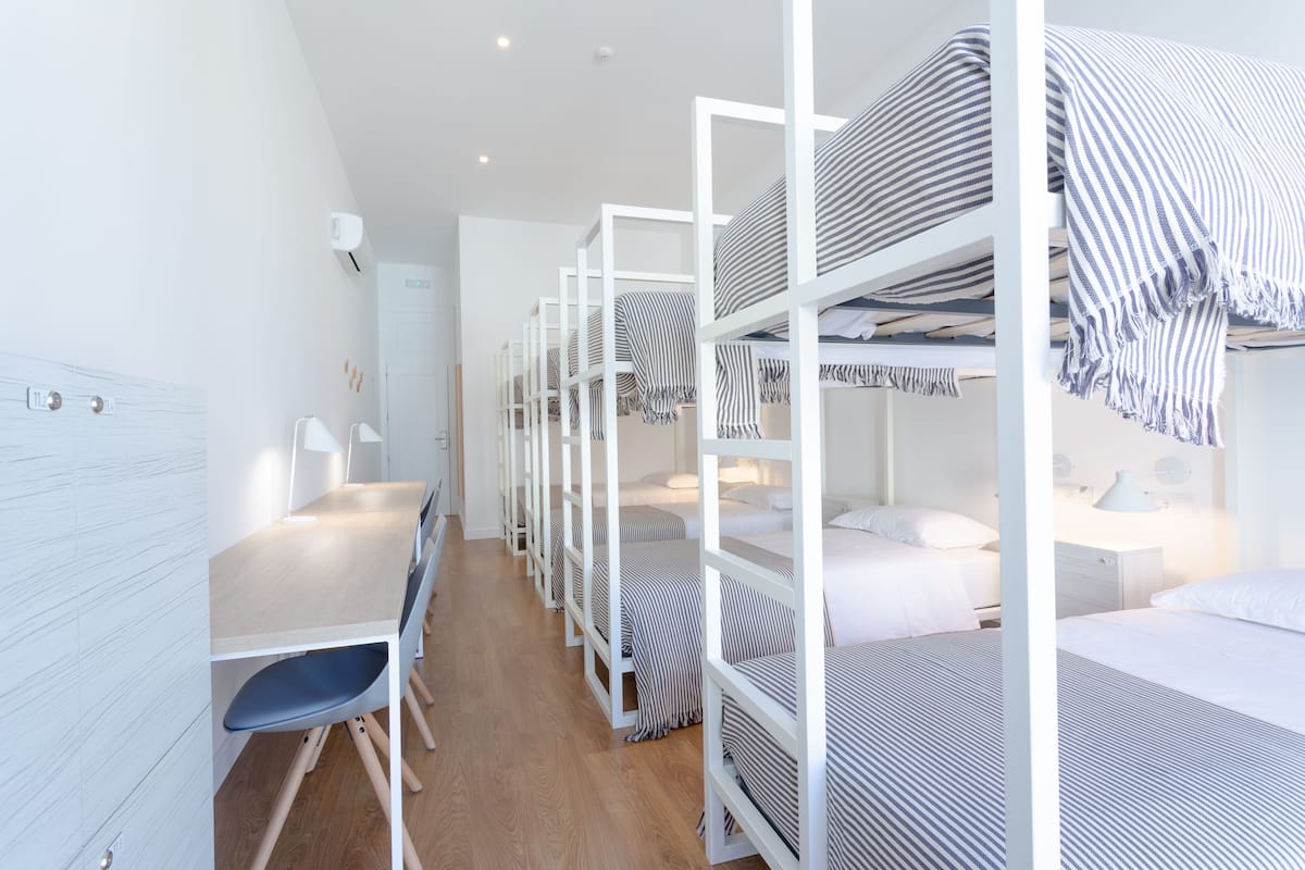 A dormitory room with bunk beds, a desk, and chairs.