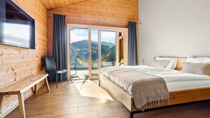 Une chambre dans une cabane en bois, avec un lit, un banc, une chaise et un hamac près d’une porte-fenêtre coulissante.