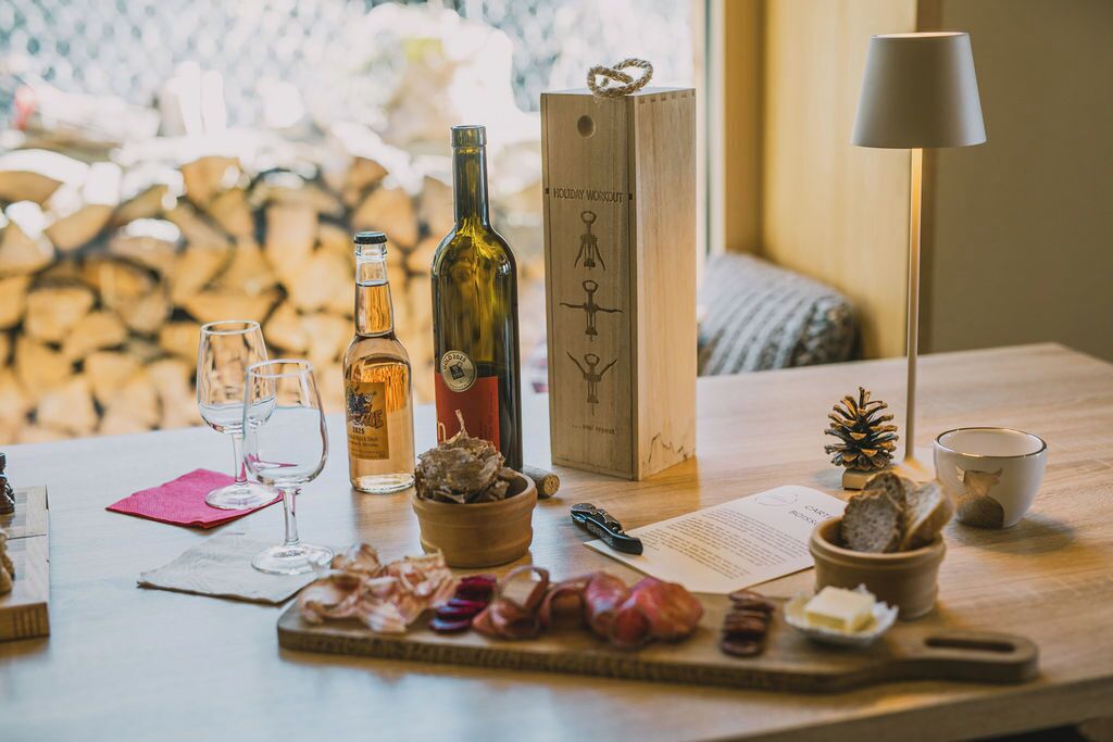 A wooden table with wine bottles, glasses, a wooden box, a lamp, and snacks.