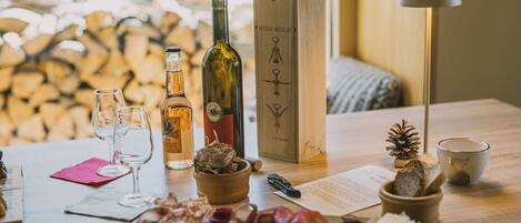 A wooden table with wine bottles, glasses, a wooden box, a lamp, and snacks.