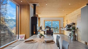 Un espace de restauration moderne, doté d’une grande table, de chaises et offrant une vue sur les montagnes grâce à de larges fenêtres.