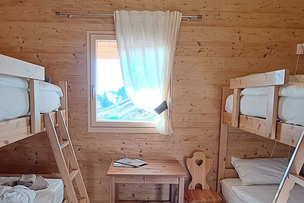 Une cabine aux murs en bois, une fenêtre avec des rideaux, un bureau et des lits superposés.