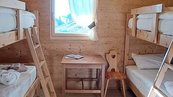 Eine Holzhütte mit Fenstern mit Vorhängen, einem Schreibtisch und Etagenbetten.