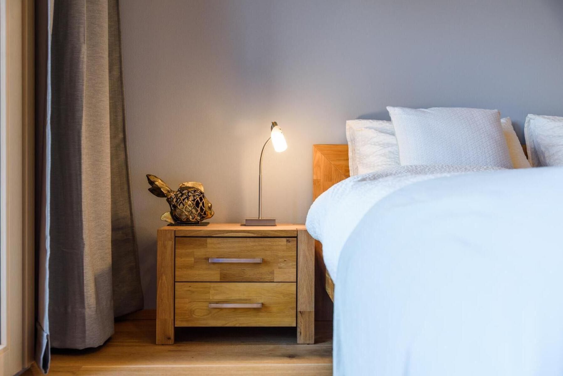 Una camera da letto con un comodino in legno, una lampada, un pesce decorativo e un letto con biancheria bianca.